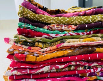 May include: A stack of colorful, patterned fabric squares. The fabrics are in shades of red, pink, orange, yellow, green, and purple. Each piece is stitched with white thread. The stack is on a light-colored surface.