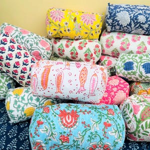 May include: A collection of colorful, patterned fabric pouches. The pouches feature floral, fish, and other designs in various colors, including pink, blue, yellow, and green. The pouches are stacked together, creating a visually appealing display.