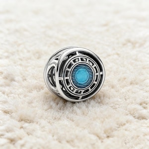 Può includere: Un charm in argento con un design circolare e un centro blu brillante. Il charm presenta intricati motivi geometrici e la parola "PANDORA" è visibile sul lato. Il charm è probabilmente realizzato in argento sterling ed è progettato per essere aggiunto a un braccialetto.
