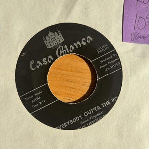 May include: A black Casa Blanca record with the song title "EVERYBODY OUT'TA THE PO" and the artist "THE LIFEGUARDS". The record has a wooden center and is on a white background. A purple sticky note is in the upper right corner.