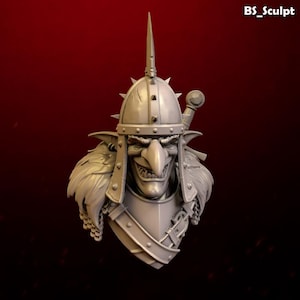 Op de afbeelding: Een lichtgrijs harsbuste van een goblin-krijger met een helm met stekels en een met bont gevoerd harnas. Het figuur heeft een lange puntige neus, een brede grijns met zichtbare tanden en een zwaardgevest op de achtergrond. Tekst BS_Sculpt is zichtbaar.