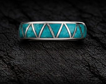 Könnte beinhalten: Ein silberner Ring mit Türkis-Inlay. Der Ring hat ein geometrisches Design mit dreieckigen silbernen Akzenten. Der Türkis hat ein gesprenkeltes Aussehen. Der Ring ist vor einem dunklen, strukturierten Hintergrund platziert.