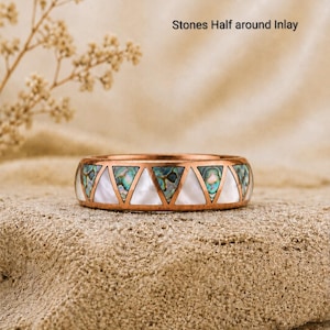 Puede incluir: Un anillo de tono cobre con una incrustación de patrón triangular repetitivo. La incrustación alterna entre concha de abulón iridiscente y nácar blanco liso. El texto "Stones Half around Inlay" es visible sobre el anillo.
