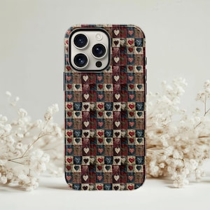 Peut inclure: Coque de téléphone avec un motif patchwork composé de carrés avec des cœurs rouges, blancs et bleus. L'étui a un bord noir et une découpe pour l'appareil photo. L'ensemble évoque un style de courtepointe.