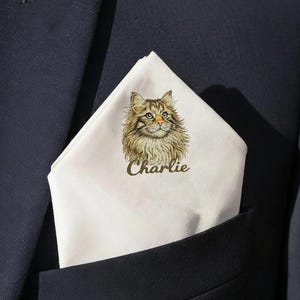 May include: A navy blue suit jacket with a white pocket square featuring a detailed illustration of a cat with the name "Charlie" printed below. The cat has brown and tan fur and green eyes.