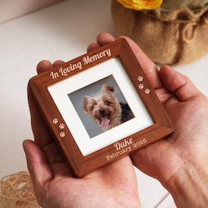 Puede incluir: Un marco de fotos cuadrado de madera con una foto de un perro. El marco está grabado con las palabras "In Loving Memory", huellas de patas, el nombre "Duke" y la fecha "Febrero 2025".