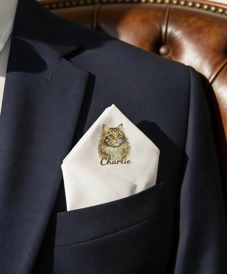 May include: A navy blue suit jacket with a white pocket square featuring a detailed illustration of a cat with the name "Charlie" printed below. The cat has brown and tan fur and green eyes.