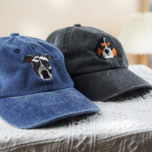 May include: Two baseball caps with embroidered dog faces. One cap is a faded blue, the other is dark gray. The dog on the blue cap has brown ears and a black and white face. The dog on the gray cap has orange and white accents.