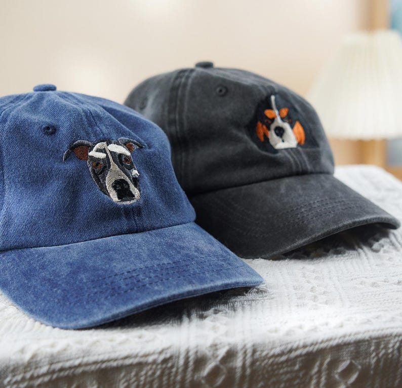 May include: Two baseball caps with embroidered dog faces. One cap is a faded blue, the other is dark gray. The dog on the blue cap has brown ears and a black and white face. The dog on the gray cap has orange and white accents.