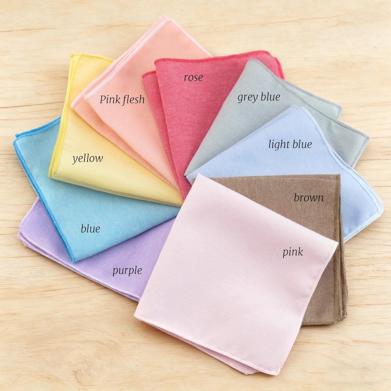 May include: A selection of colourful handkerchiefs arranged in a fan. The handkerchiefs are in shades of yellow, pink, blue, and purple, with colour names printed on them. The fabric looks to be a smooth, lightweight material.