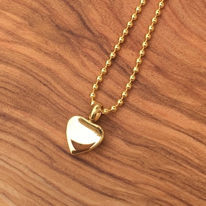 May include: A gold heart-shaped pendant necklace with a ball chain.
