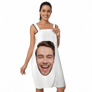 May include: White, sleeveless dress featuring a large, smiling face print. The dress has black trim on the straps and a knee-length hemline. The person is holding the dress open.