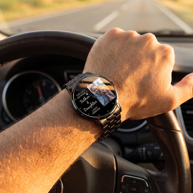 May include: A black wristwatch with a metal band displays a photo of a father and daughter. The watch face has the text "The Love Between a Father & Daughter Lasts Forever."