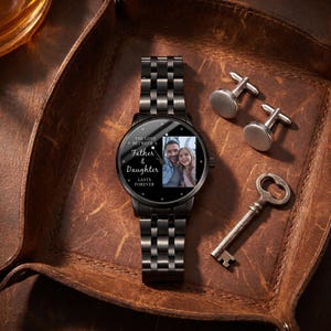 May include: A black wristwatch with a photo of a father and daughter on the face, along with the text "The Love Between a Father & Daughter Lasts Forever." The watch is accompanied by silver cufflinks and a vintage key.