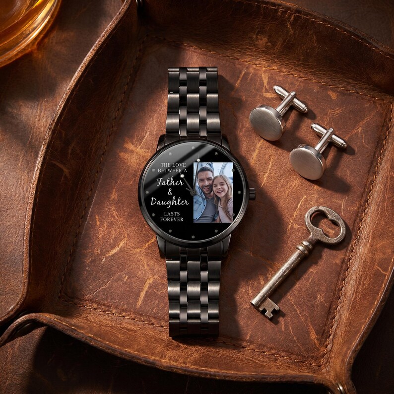 May include: A black wristwatch with a photo of a father and daughter on the face, along with the text "The Love Between a Father & Daughter Lasts Forever." The watch is accompanied by silver cufflinks and a vintage key.