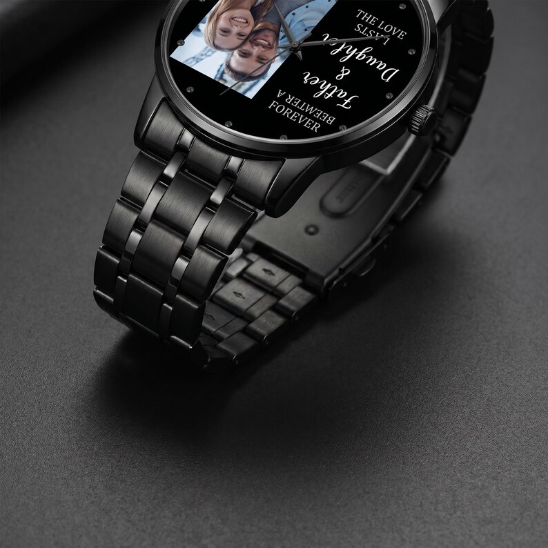 May include: Black wristwatch with a black metal band. The watch face features a photo of a couple and the words "Daughter & Father Forever" and "The Love Lasts". The watch is on a dark surface.