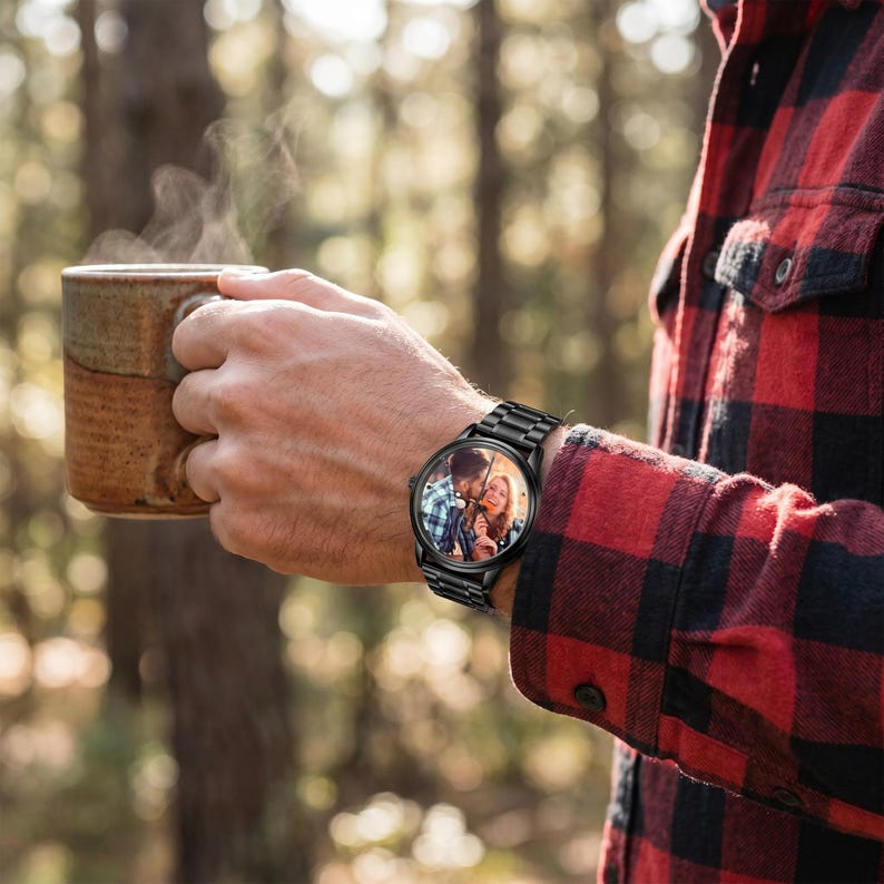 K&ouml;nnte beinhalten: Schwarze Armbanduhr mit einem Foto eines Paares auf dem Zifferblatt. Die Uhr hat ein schwarzes Metallarmband. Die Person tr&auml;gt ein rot-schwarz kariertes Hemd und h&auml;lt einen braunen Becher. Der Hintergrund ist ein verschwommener Wald.