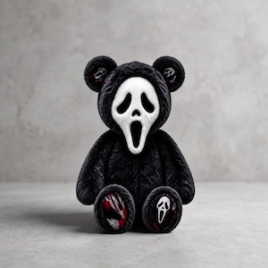 May include: A plush teddy bear featuring a black fuzzy body and a white Ghostface mask covering its face. The bear has matching black ears with small mask details inside, and the soles of its feet feature red and black patterns with a mask icon.