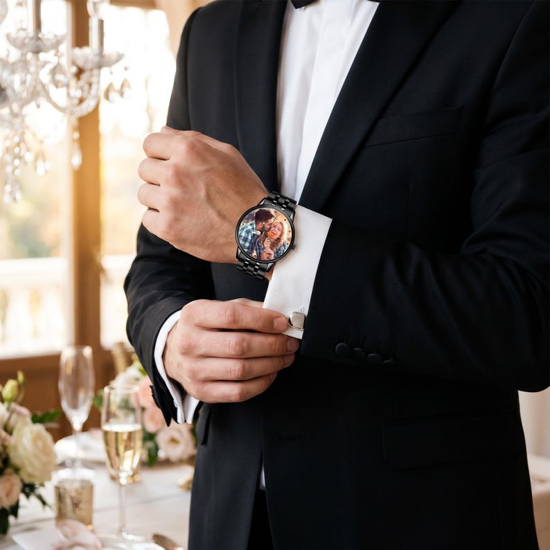 K&ouml;nnte beinhalten: Schwarze Armbanduhr mit einem Foto auf dem Zifferblatt, getragen an einem Handgelenk mit wei&szlig;er Manschette und silbernem Manschettenknopf. Die Uhr hat ein schwarzes Metallarmband. Die Person tr&auml;gt einen schwarzen Anzug. Das Zifferblatt zeigt ein Farbfoto eines Paares.