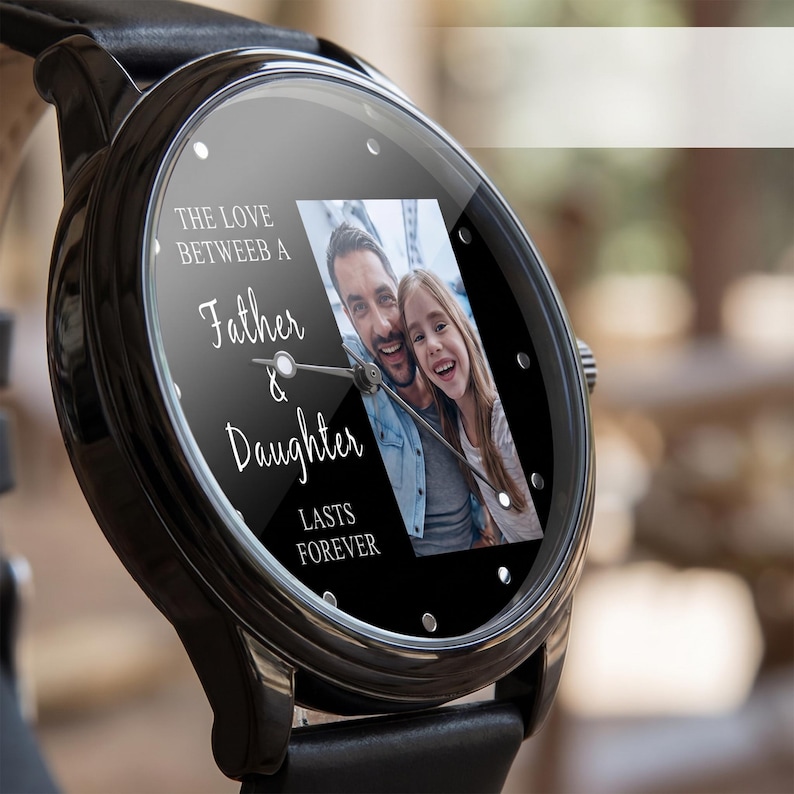 May include: Black wristwatch with a leather band. The watch face displays a photo of a father and daughter, with the text "THE LOVE BETWEEN A Father & Daughter LASTS FOREVER". The watch has silver accents.