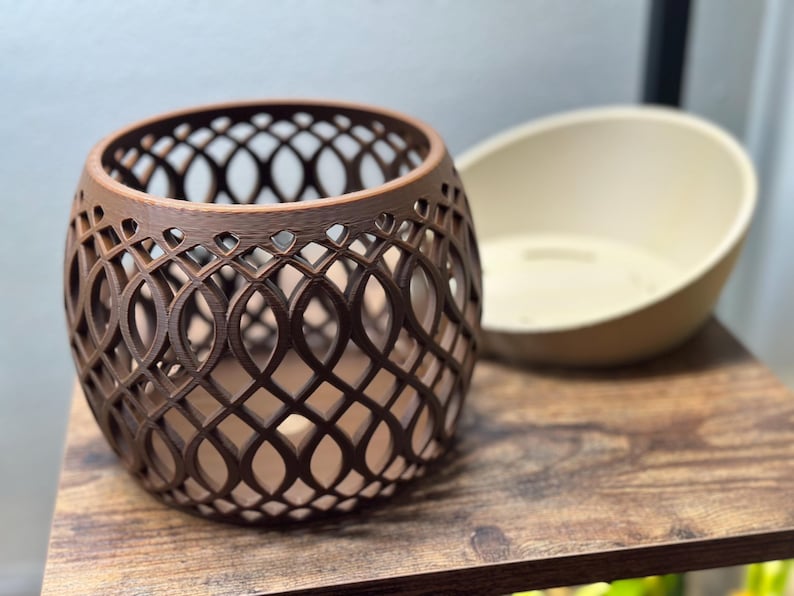 May include: A brown, openwork, spherical decorative object with a repeating oval pattern. Beside it is a cream-colored, oval-shaped bowl. Both items are on a wooden surface.