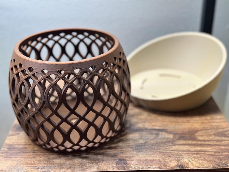 May include: A brown, openwork, decorative vase with an intricate pattern, next to a cream-colored, oval-shaped bowl. The vase has a rounded shape and is made of a dark brown material. The bowl is smooth and has a simple design.