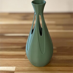 A green vase with a unique, sculptural design sits on a wooden surface.