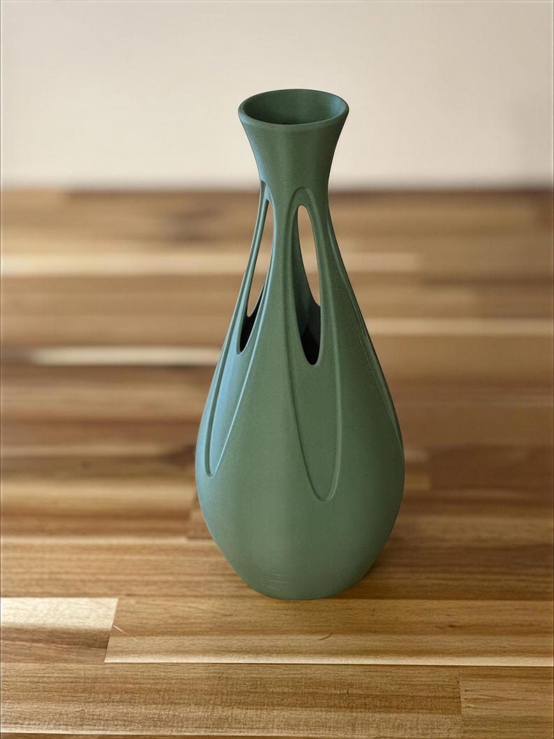 A green vase with a unique, sculptural design sits on a wooden surface.