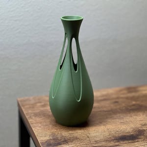 A green vase with a unique, geometric design sits on a wooden table.