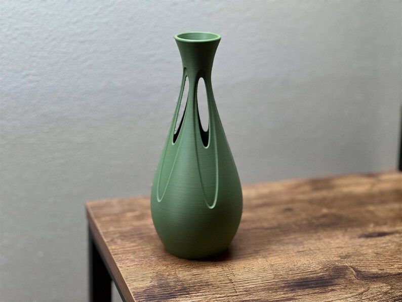 A green vase with a unique, geometric design sits on a wooden table.
