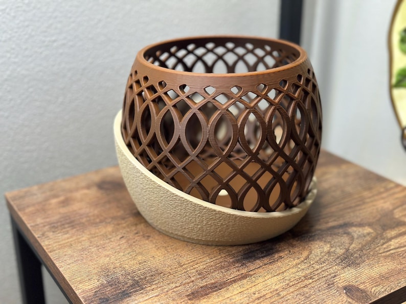 May include: A brown, openwork decorative planter with a geometric design. The planter sits on a beige, textured saucer. The planter is on a wooden table.