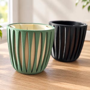 May include: Two plant pots with a dual-layer design. The front pot is sage green with a cream-colored inner liner, while the back pot is solid black. Both feature a vertical, slatted outer shell with a rounded base and an open top.