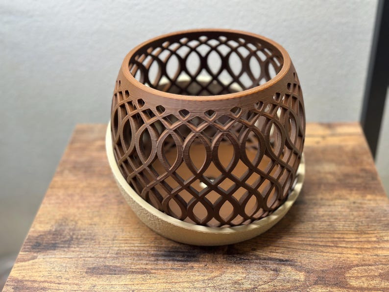 May include: A brown, openwork planter with a decorative oval pattern. The planter sits on a cream-colored saucer. The design allows for air circulation and drainage, suitable for small plants or succulents.
