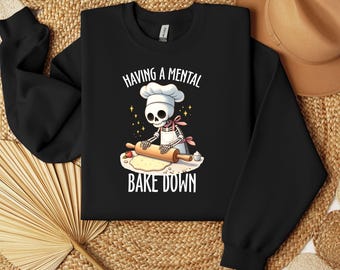 May include: Black sweatshirt with a graphic of a skeleton chef rolling dough with a rolling pin. The text "HAVING A MENTAL BAKE DOWN" is above and below the graphic. The skeleton wears a chef's hat and apron.