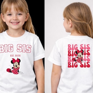 Pu&ograve; includere: Una t-shirt bianca a maniche corte con una grafica rossa di Minnie Mouse e il testo BIG SIS EST. 2026 sul davanti. Il retro della maglietta mostra il testo BIG SIS ripetuto in un carattere ondulato rosso e rosa con Minnie Mouse.