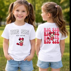 Pu&ograve; includere: Una t-shirt bianca a maniche corte con il testo BIG SIS EST. 2026 e una grafica di Minnie Mouse sul davanti. Il retro mostra il testo BIG SIS ripetuto in rosa e rosso con una grafica centrale di Minnie Mouse con un vestito a pois rossi.