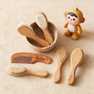 Könnte beinhalten: Eine Sammlung von Baby-Pflegeartikeln, darunter Holzbürsten und ein Kamm, einige mit dem Aufdruck "Avery". Ein kleines, gelbes Spielzeug in Form eines Affen ist ebenfalls vorhanden. Die Bürsten haben weiche Borsten, und der Kamm hat feine Zähne.