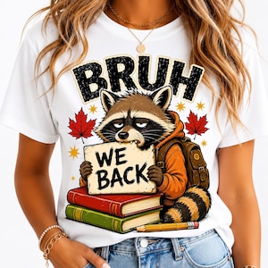 Pode incluir: Uma t-shirt branca com um gráfico de um guaxinim vestindo um capuz laranja e uma mochila. O guaxinim segura uma placa que diz "BRUH WE BACK" acima de dois livros empilhados e um lápis, rodeado por folhas de bordo vermelhas e estrelas.
