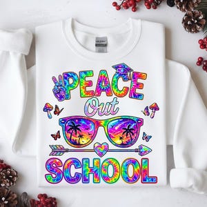 以下が含まれることがあります： カラフルなタイダイデザインの白いスウェットシャツ。グラフィックには、「PEACE OUT SCHOOL」の文字と、ビーチの風景、蝶、キノコを映し出すサングラスが含まれています。ピースサインと卒業キャップも含まれています。
