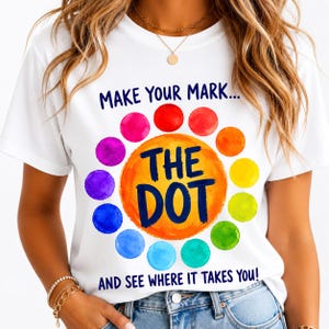 May include: A white short-sleeved t-shirt featuring a colorful graphic of a large orange circle surrounded by smaller watercolor-style dots in a rainbow spectrum. The text reads "MAKE YOUR MARK... THE DOT AND SEE WHERE IT TAKES YOU!" in dark blue.