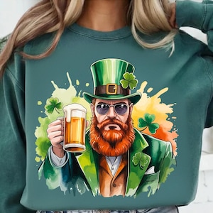 Puede incluir: Sudadera verde con un diseño del Día de San Patricio. El gráfico representa a un hombre con barba roja, gafas de sol y sombrero verde, sosteniendo una jarra de cerveza. El diseño incluye tréboles y salpicaduras de pintura coloridas.