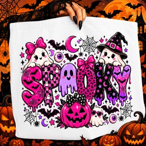 Può includere: Una borsa tote bianca con una grafica colorata che riporta la parola SPOOKY in grandi lettere stilizzate. Il design include fantasmi rosa e viola, una zucca, pipistrelli, ragnatele, bulbi oculari e stelle in un vivace tema di Halloween.