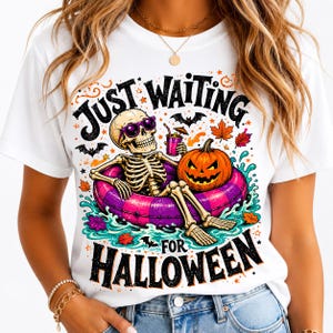 May include: A white t-shirt featuring a graphic of a skeleton wearing purple sunglasses, relaxing in a pink and purple striped pool float. The skeleton holds a drink with a tiny umbrella next to a jack-o'-lantern. Text reads Just Waiting For Halloween.
