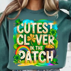 Puede incluir: Sudadera verde azulado con un gráfico colorido. El gráfico presenta el texto "Cutest Clover in the Patch" en letras doradas, junto con un arcoíris, tréboles, una olla de oro y sombreros de duende. Ideal para el Día de San Patricio.