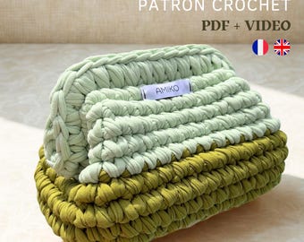 May include: A handmade crochet makeup bag or clutch in shades of green. The bag is made with thick yarn, featuring a textured stitch pattern. The text "MAKEUP BAG / CLUTCH PATRON CROCHET PDF + VIDEO" is displayed at the top.