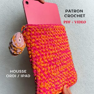 May include: A handmade crochet iPad case in vibrant shades of pink and orange. The case features a textured stitch pattern and includes a matching keychain. Text on the image reads "PATRON CROCHET PDF + VIDEO" and "HOUSSE ORDI / IPAD".