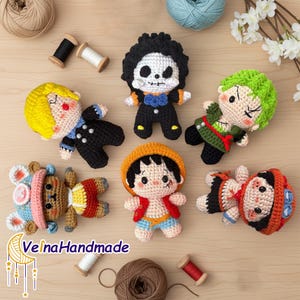 Peut inclure: Collection de poupées crochetées à la main, représentant différents personnages avec des couleurs de cheveux et des tenues distinctes. Les poupées sont disposées sur une surface en bois avec de la laine et des bobines de fil, mettant en valeur un thème artisanal.