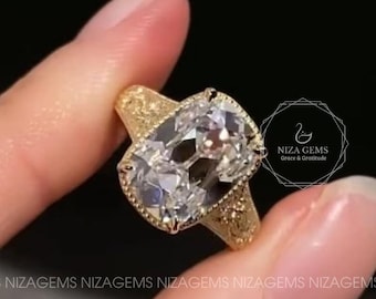 May include: A gold ring featuring a large, clear, rectangular-cut gemstone. The ring has a detailed, textured band and a halo of smaller stones around the main gem. The ring is held up against a dark background.