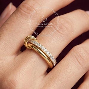Puede incluir: Un anillo de oro con un diseño de nudo, con una banda de pequeñas piedras preciosas transparentes. El anillo se lleva en un dedo, con el nombre de la marca "Niza Gems" visible en el fondo. Es una joya.
