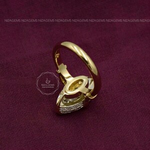 May include: A gold ring featuring a central marquise-cut gemstone and a band accented with small pav&eacute;-set diamonds. The ring displays the NIZA GEMS logo and text on the side, with a smooth, polished gold finish throughout the band.